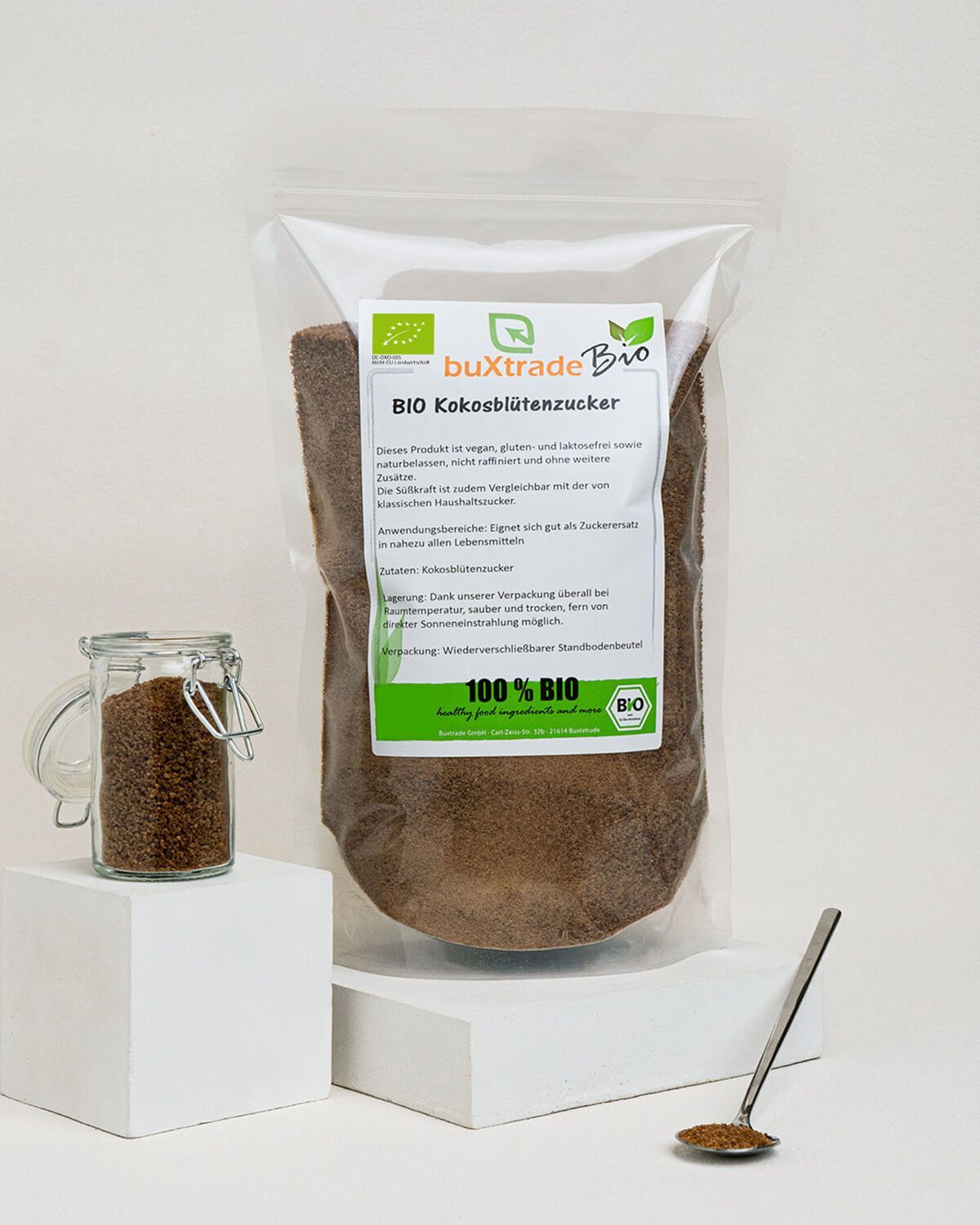 Bio Kokosblütenzucker in transparenter Standbodenbeutel-Verpackung, daneben ein Glas mit Zucker und ein Löffel.