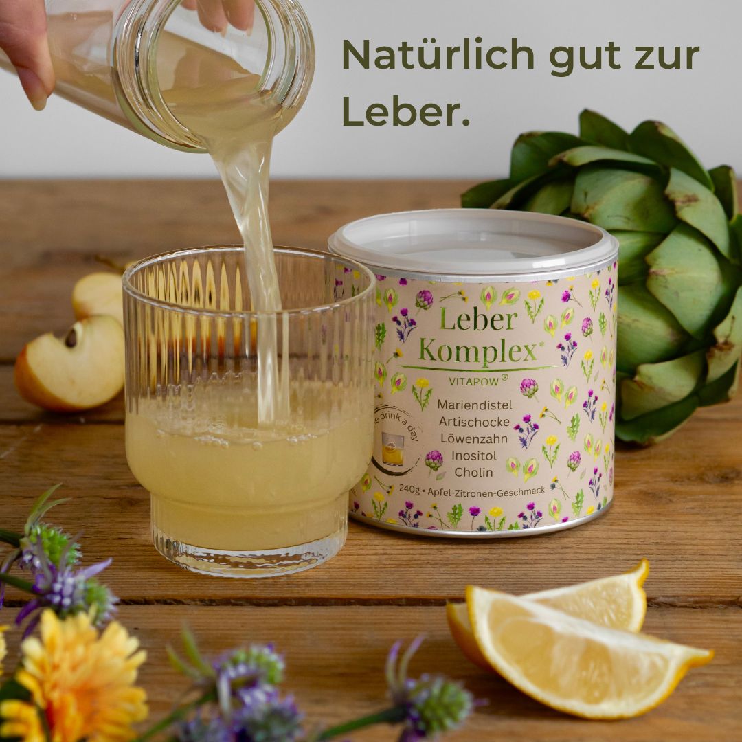 Glas wird mit gelber Flüssigkeit gefüllt. Daneben Dose mit Produktnamen und Zutaten. Zitronen und Artischocke.