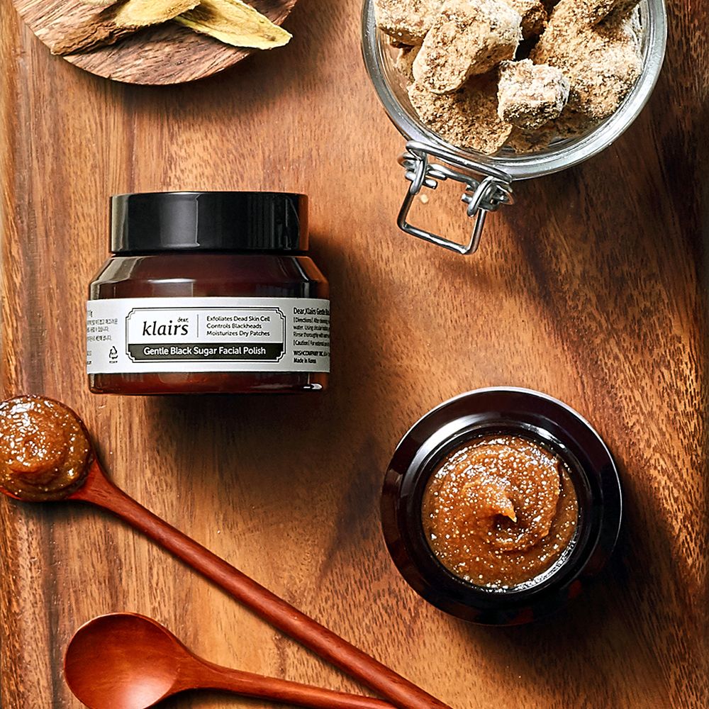Klairs Gentle Black Sugar Facial Polish auf einem Holztisch mit Zutaten wie braunem Zucker.