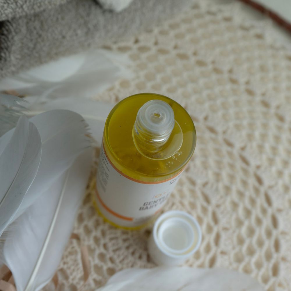 Nahaufnahme der geöffneten Babyöl-Flasche. Der Deckel liegt daneben. Gelbe Flüssigkeit sichtbar.