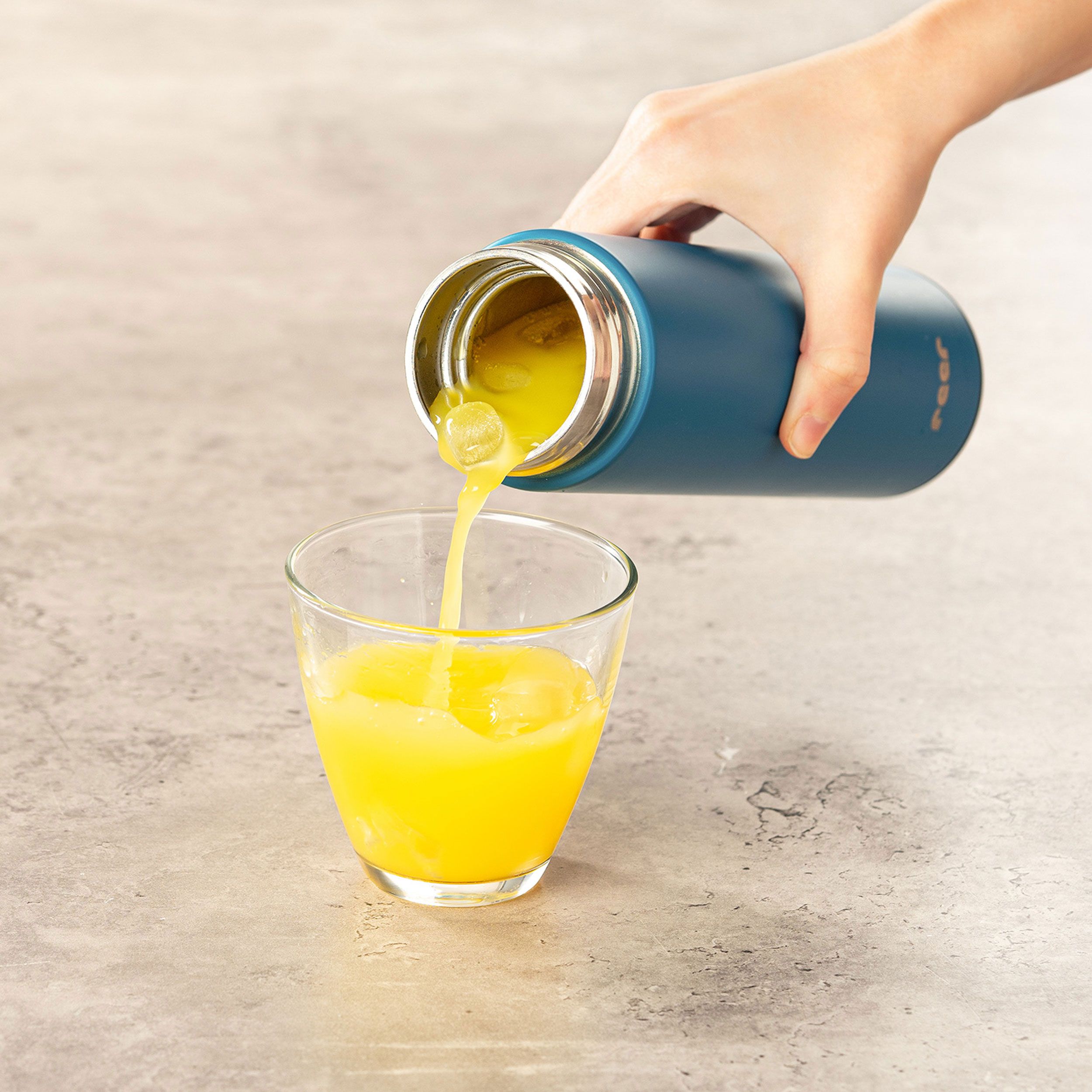 Blaue Isolierflasche gießt Flüssigkeit in ein Glas. Markenlogo sichtbar. Auf Tisch.