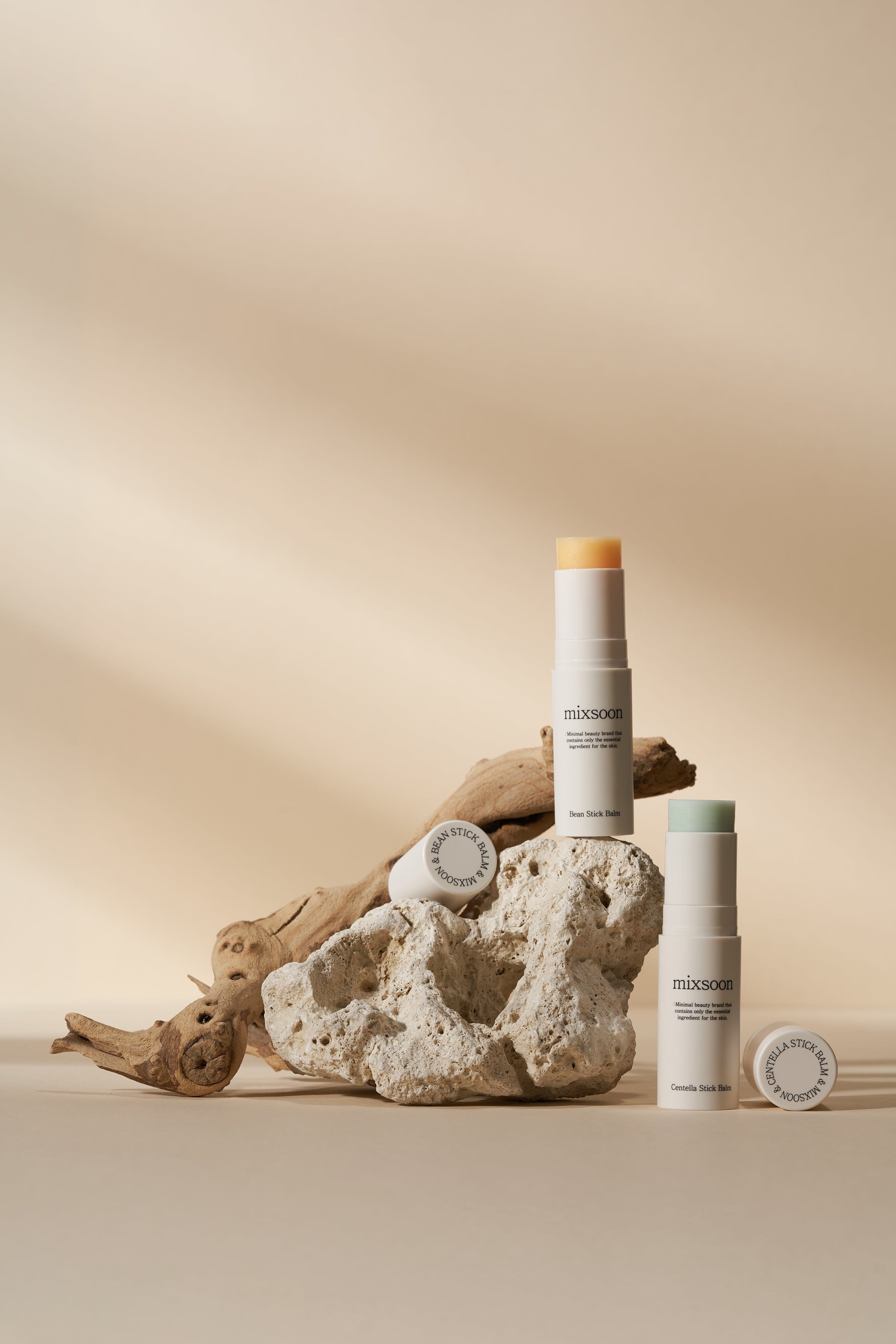 Drei Stick-Balsame auf einem Stein und Holz. Zwei mit Kappen, einer offen. Aufschrift: mixsoon Centella Stick Balm.