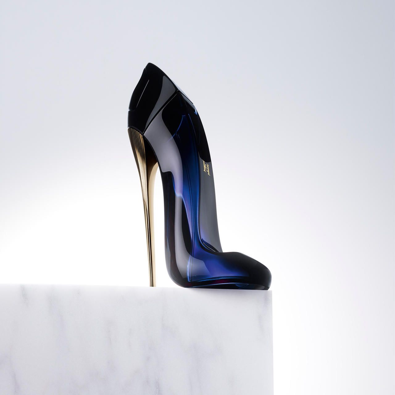 Blauer Flakon in Schuhform mit goldenem Absatz. Auf weißem Podest.