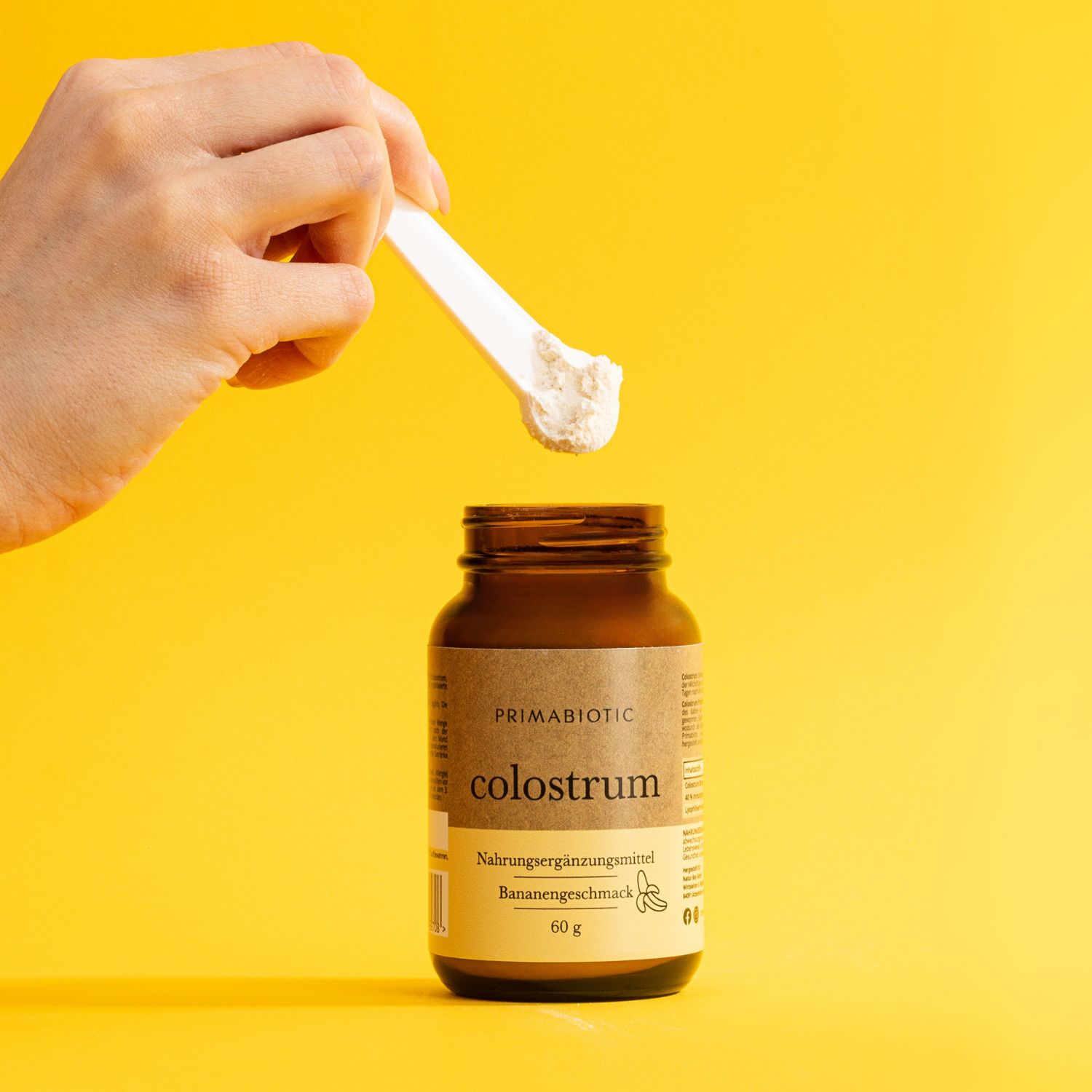 Braune Glasflasche mit schwarzem Deckel. Produktname, Bananengeschmack und 60g. Weiße Pulver wird mit einem Löffel entnommen.