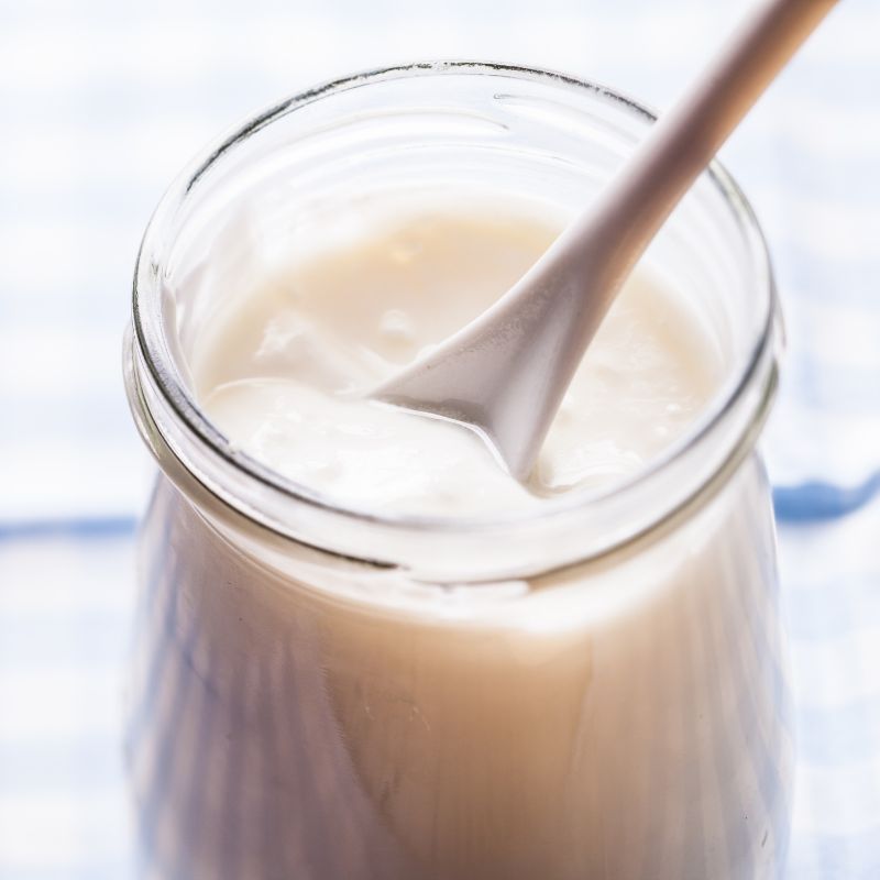 Glas mit Joghurt und Löffel. Nahaufnahme. Blauer karierter Hintergrund.