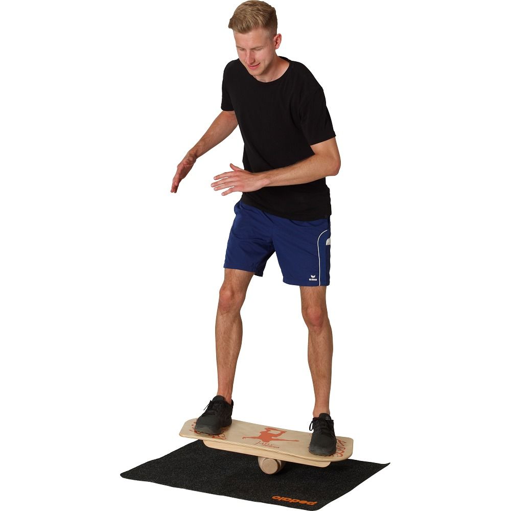 Mann steht auf einem Balance Board. Das Board liegt auf einer schwarzen Matte mit Logo. Der Mann hat die Arme erhoben.