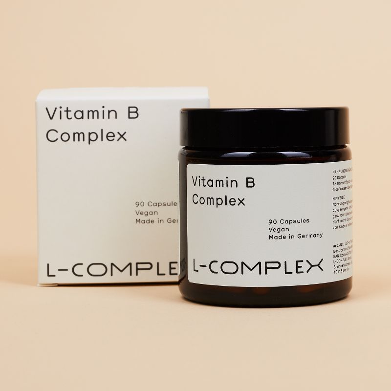 Braune Glasdose und weiße Schachtel. Dose mit "Vitamin B Complex", "90 Capsules", "Vegan", "L-COMPLEX".