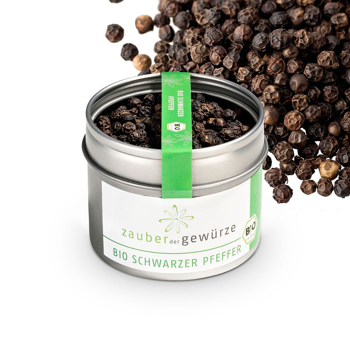 Geöffnete Dose Bio Schwarzer Pfeffer. Silberne Dose mit Etikett und grünem Band. Pfefferkörner daneben. Aufschrift: Zauber der Gewürze, Bio Schwarzer Pfeffer.