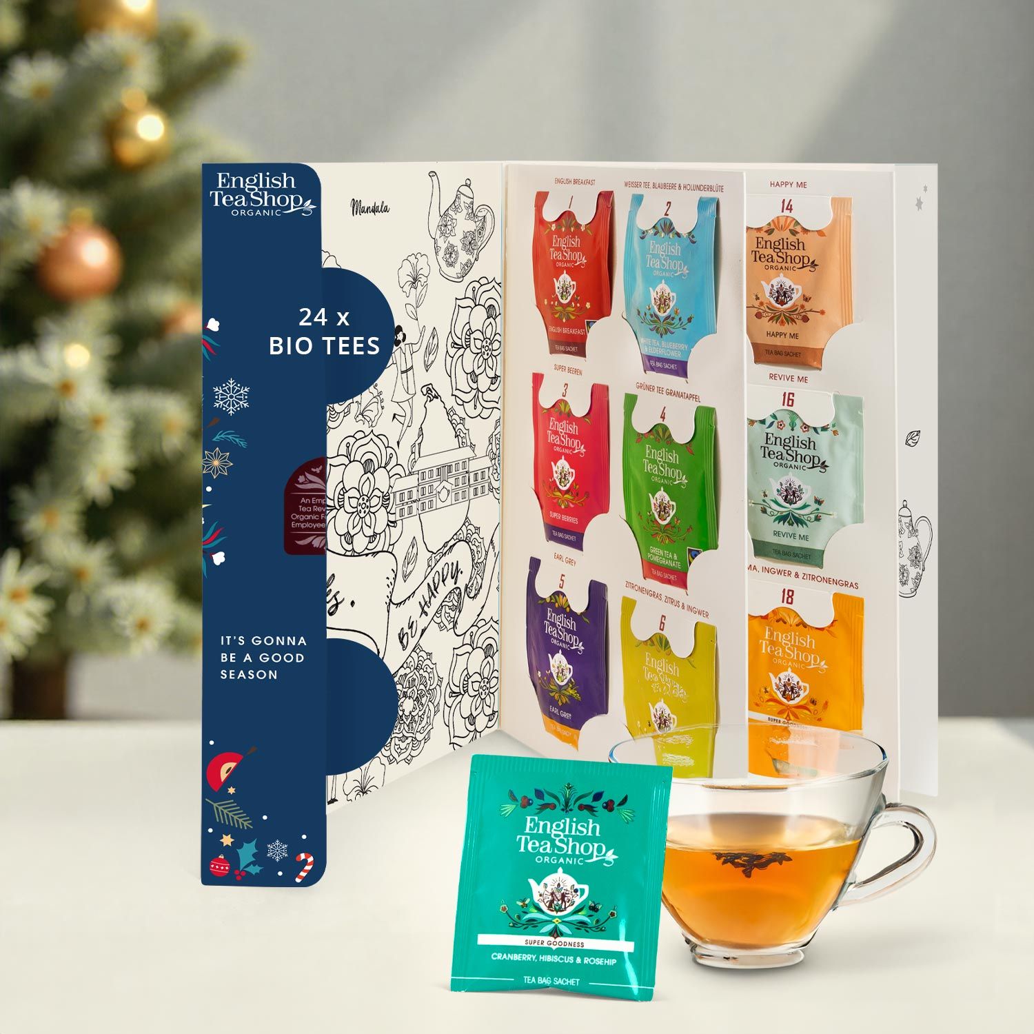 Adventskalender mit 24 Bio-Teesorten, geöffnet. Teebeutel in verschiedenen Farben. Einzelner Teebeutel und Teetasse daneben. Mit Illustrationen.