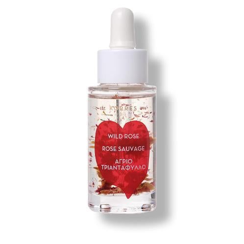 Klarflüssiges Öl in Glasflasche mit Pipette. Roter Herzaufkleber mit Text. Blütenblätter im Öl.