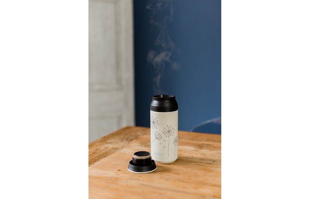 Thermosflasche mit Pusteblumen-Design, Deckel daneben. Dampf steigt auf. Auf Tisch platziert.