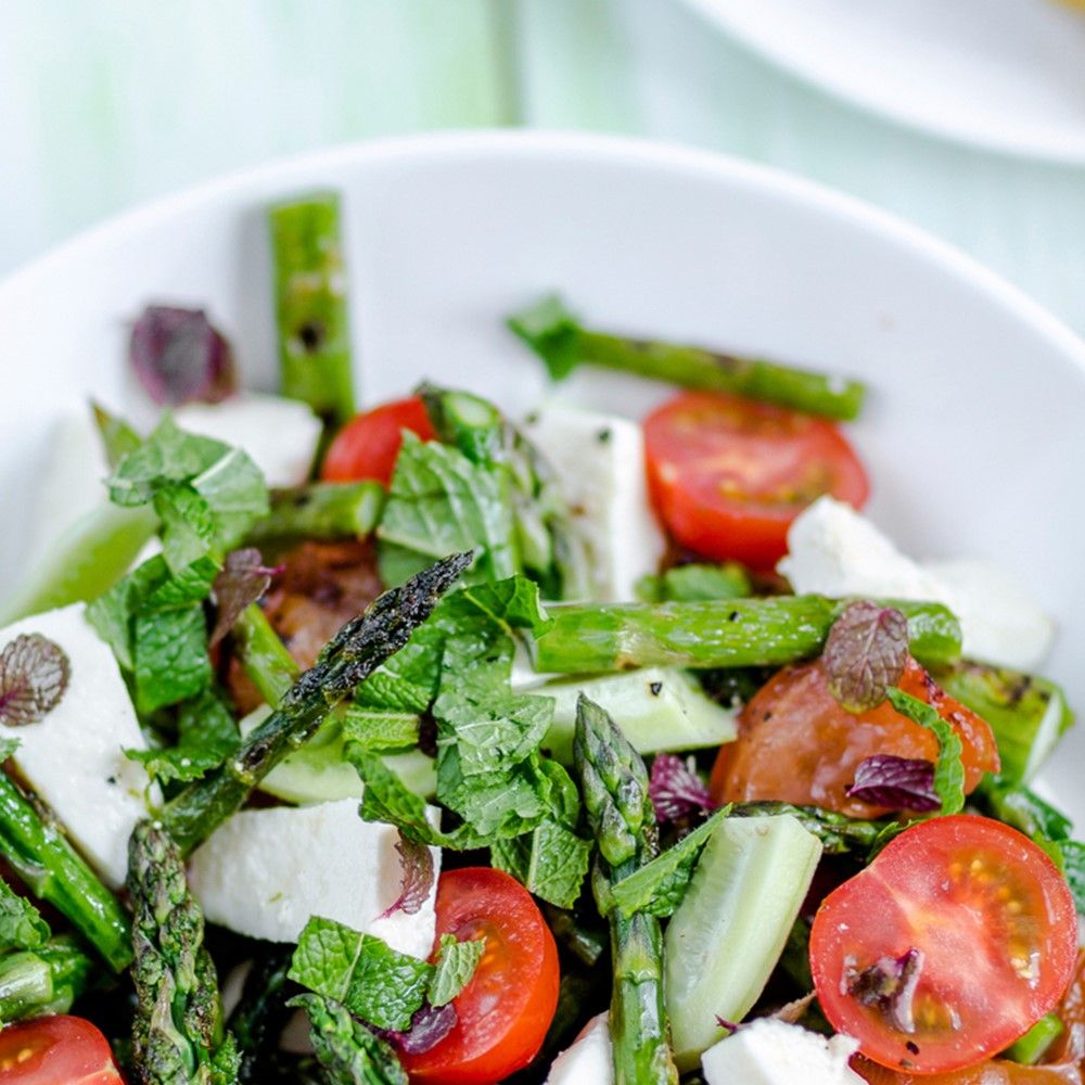 Salat mit Spargel, Tomaten, Käse und Kräutern in weißer Schüssel. Nahaufnahme.