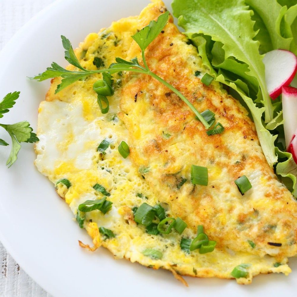 Omelett auf weißem Teller. Garniert mit Petersilie und Frühlingszwiebeln. Beilagen: Salat und Radieschen.