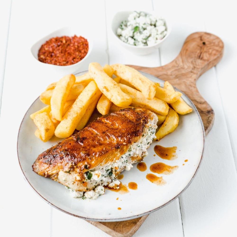 Teller mit Hähnchenbrust, Pommes und Beilagen. Gebratene Hähnchenbrust gefüllt, Pommes, Beilagen in Schalen, Holzbrett.
