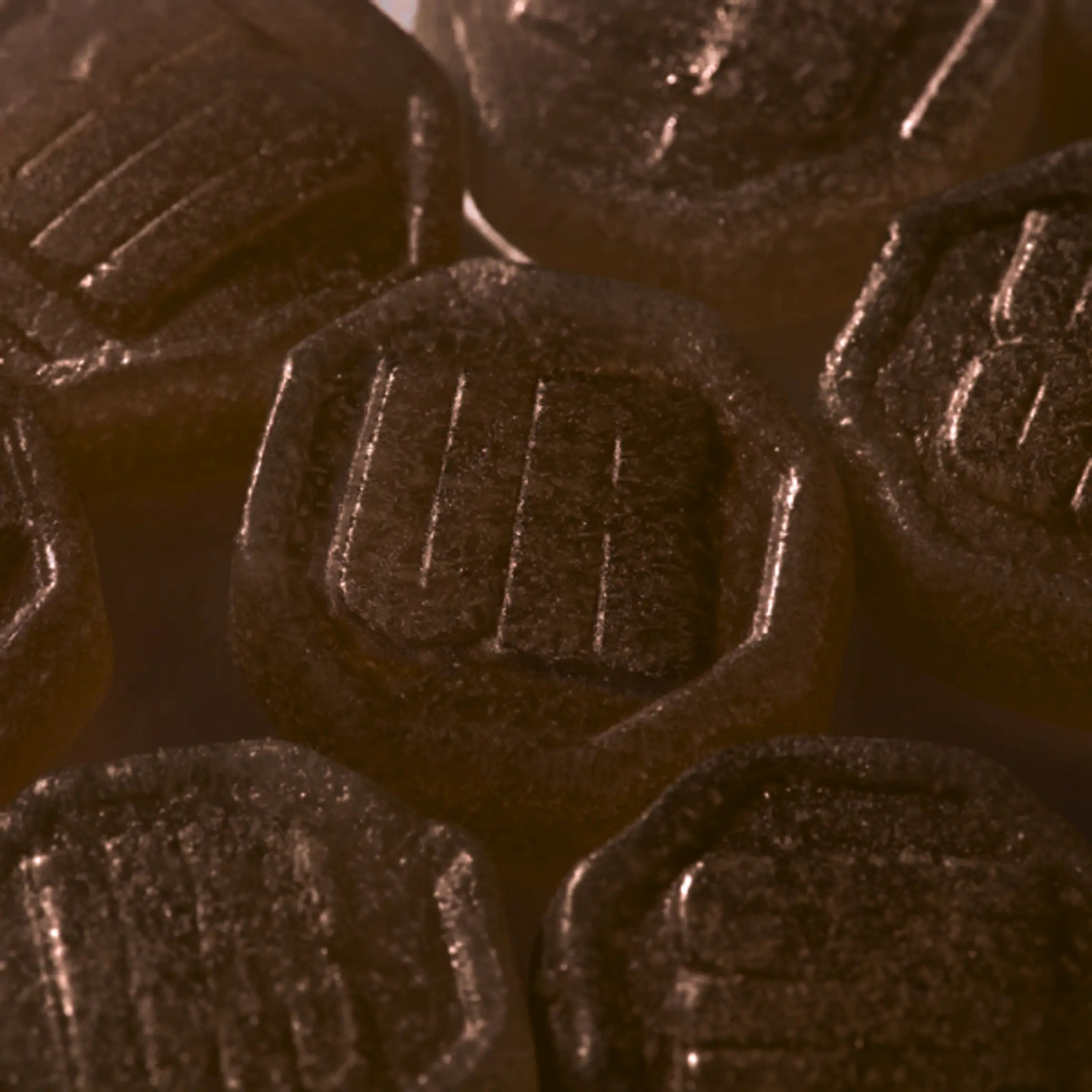 Braune, sechseckige Gummies mit Prägung. Einzelne Gummies sind sichtbar.