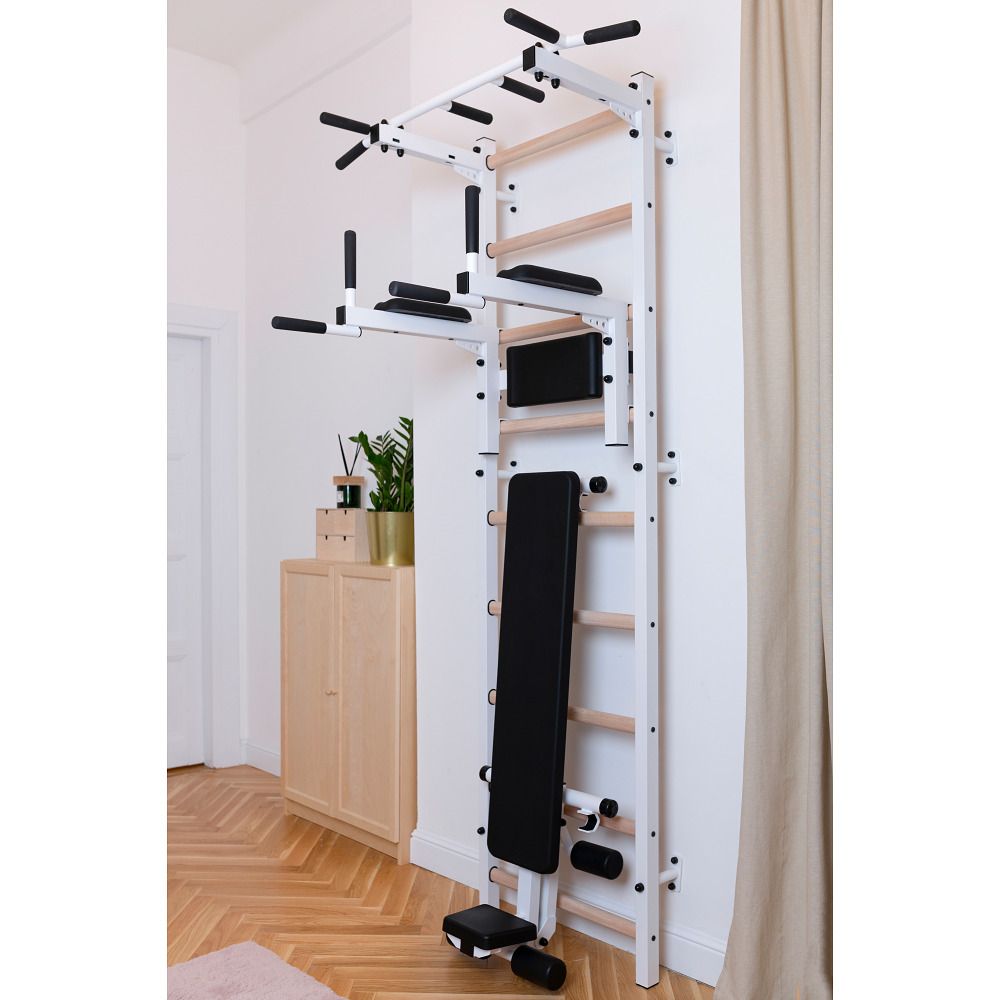 Fitness-System an Wand montiert. Sprossenwand, Klimmzugstange, Dip-Barren und Trainingsbank. Holz- und Metallkonstruktion. In Wohnraum.