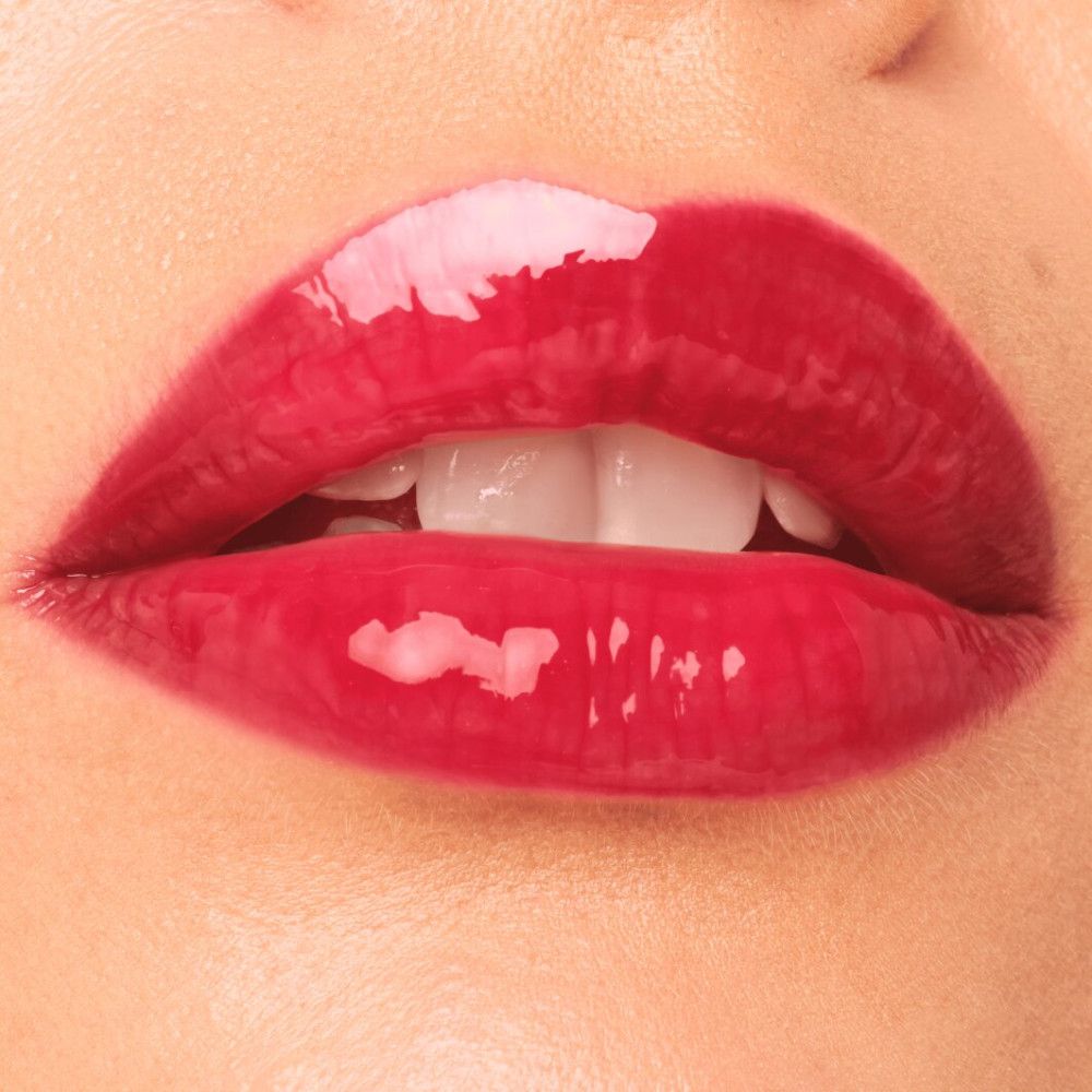 Nahaufnahme von Lippen mit glänzendem, rotem Lippenfiller Gloss. Offener Mund, Zähne sichtbar.