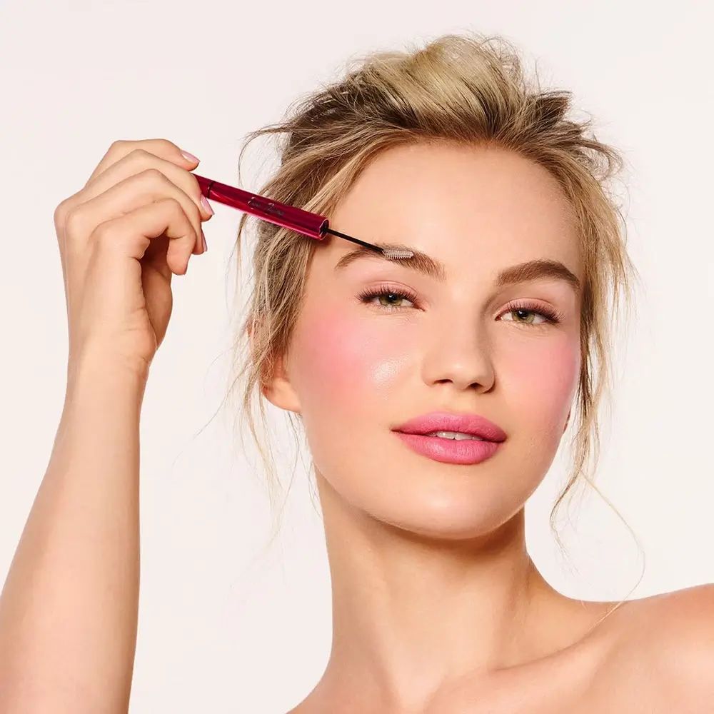 Frau mit rosa Wangen und Lippen. Sie benutzt einen Augenbrauenstift. Der Stift ist rot.