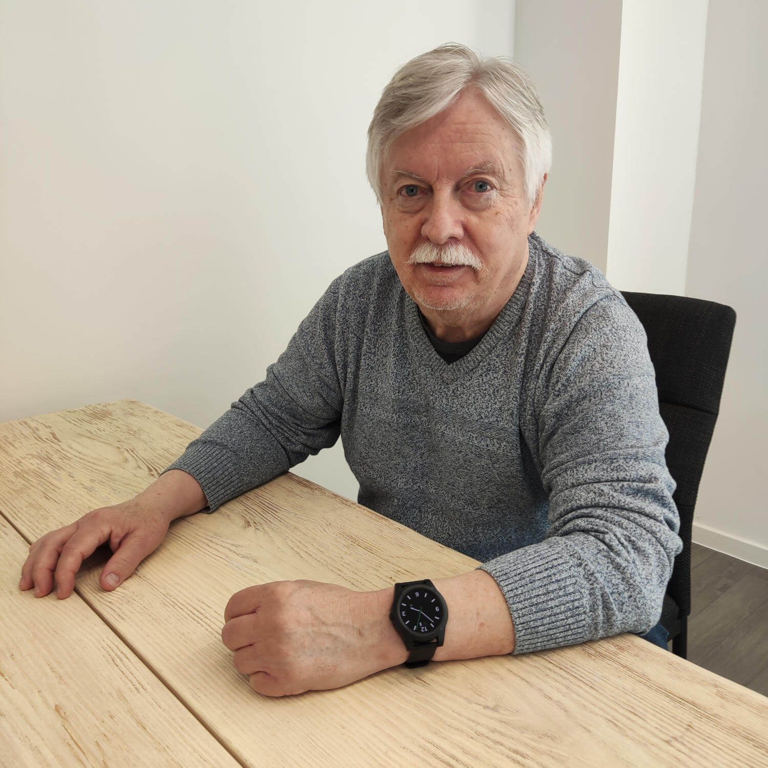 Mann mit grauer Kleidung trägt eine schwarze Smartwatch am Handgelenk.