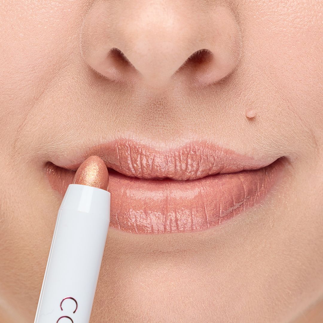 Lippenstift wird auf Lippen aufgetragen. Der Stift hat eine weiße Hülle und eine rosafarbene Spitze. Die Lippen sind leicht geöffnet.