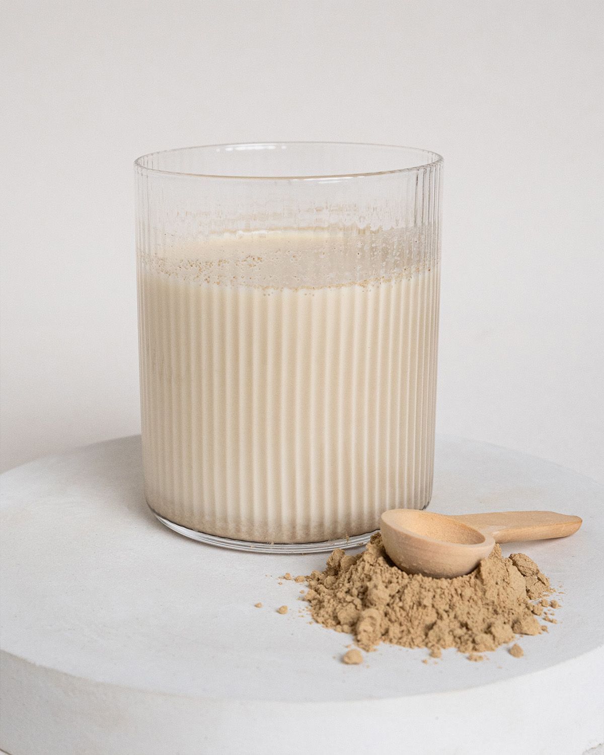 Glas mit Flüssigkeit und braunem Pulver. Ein Holzlöffel liegt neben dem Pulver. Geriffeltes Glas.