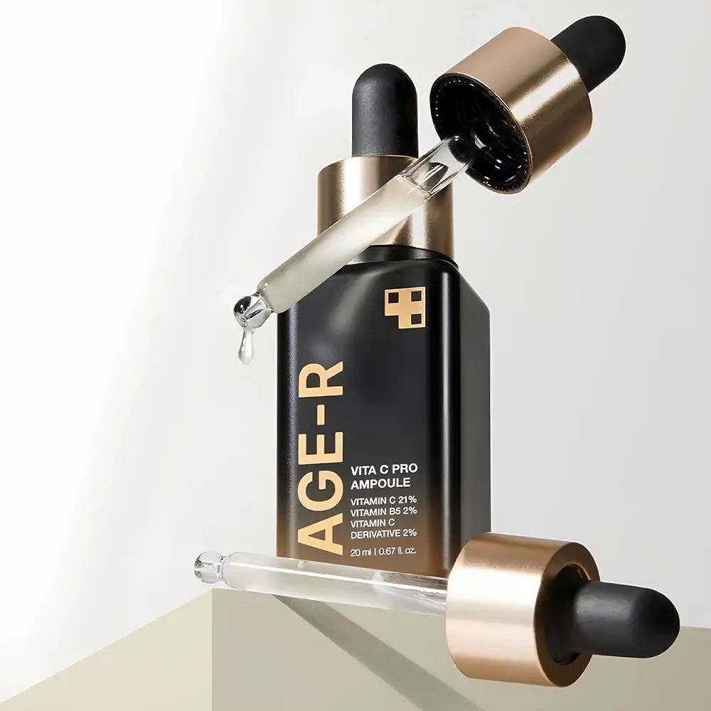 Serumflasche mit goldfarbenem Deckel und Pipette. Zwei Pipetten liegen daneben. Aufschrift AGE-R Vita C Pro Ampoule.