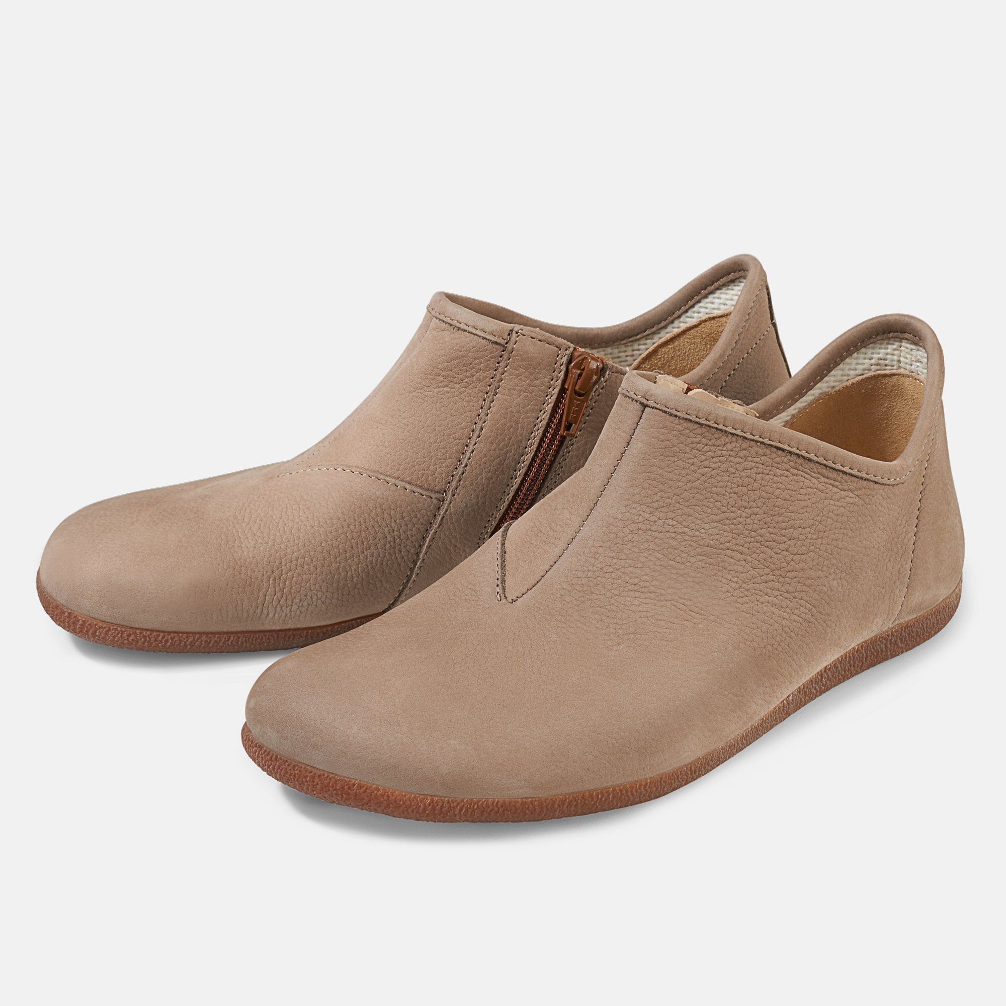 Beige Slipper mit seitlichem Reißverschluss. Flache Sohle, breite Passform. Zwei Schuhe nebeneinander.