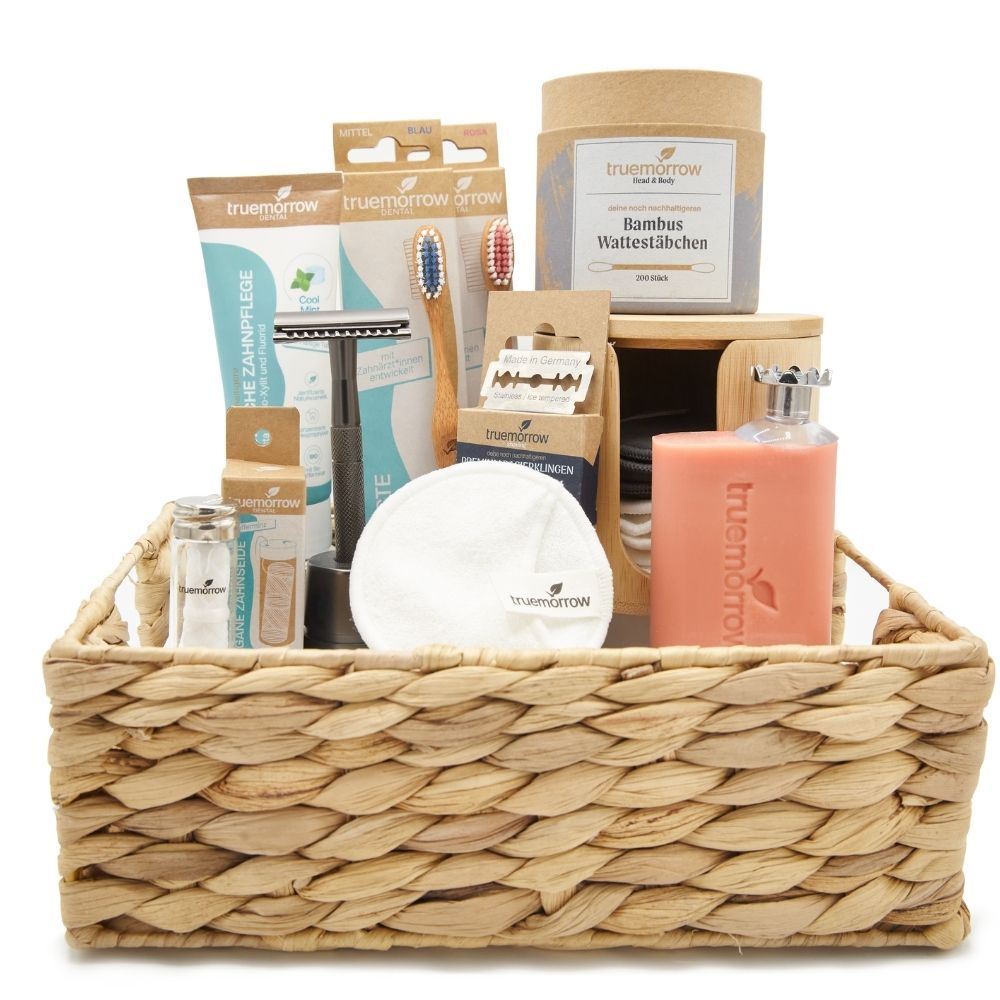 Geschenkset mit Rasierer, Zahnbürsten, Abschminkpads, Wattepads, Seife und Rasierklingen in einem Korb.