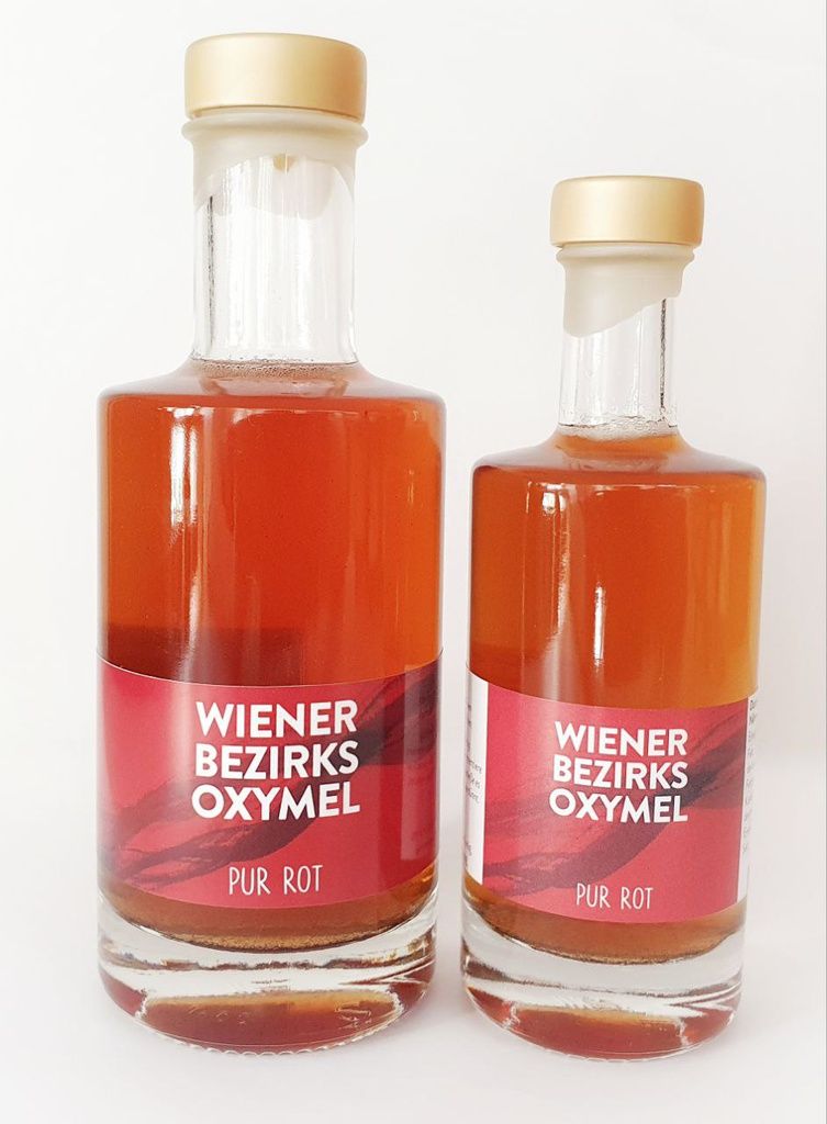 Zwei Glasflaschen mit roter Flüssigkeit und Etikett "Wiener Bezirks Oxymel Pur Rot". Goldfarbene Verschlüsse.