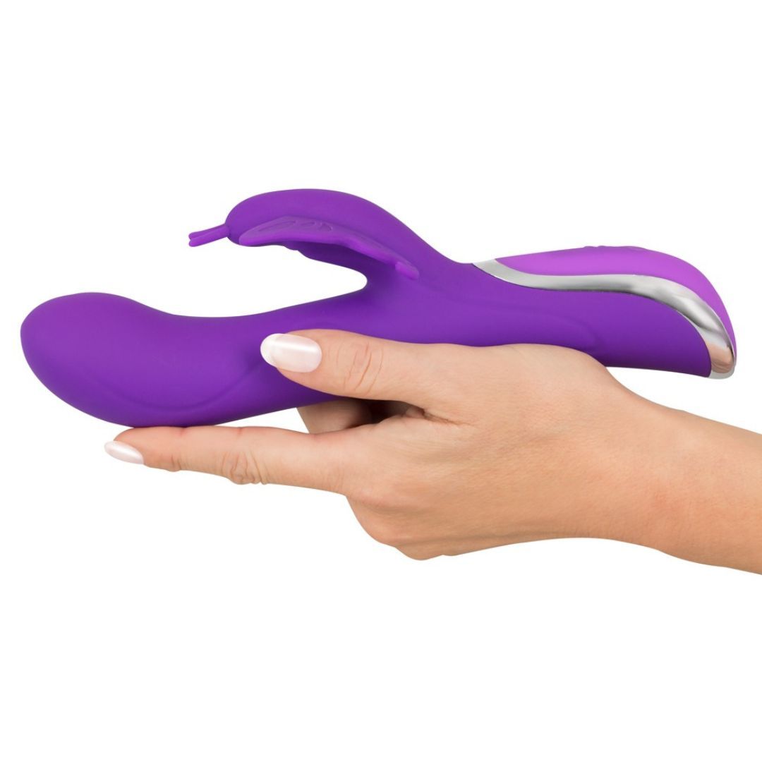 Lila Vibrator, gehalten in einer Hand. Schmetterlings-Klitorisreizer, gebogene Form, silberne Akzente.