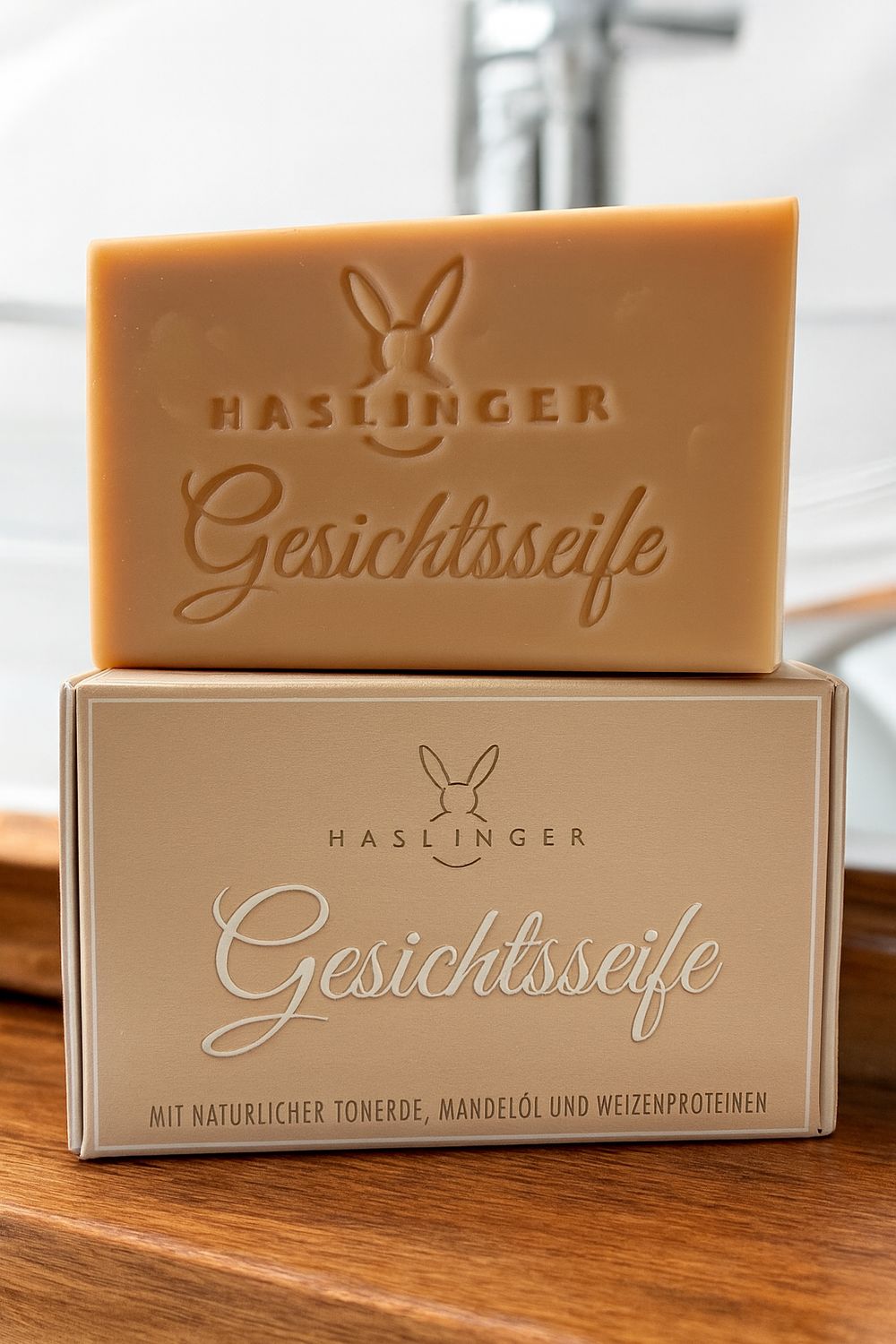 Seifenstück und Verpackung. Auf der Seife und der Verpackung steht "Haslinger Gesichtsseife". Auf der Verpackung steht "mit natürlicher Tonerde, Mandelöl und Weizenproteinen".