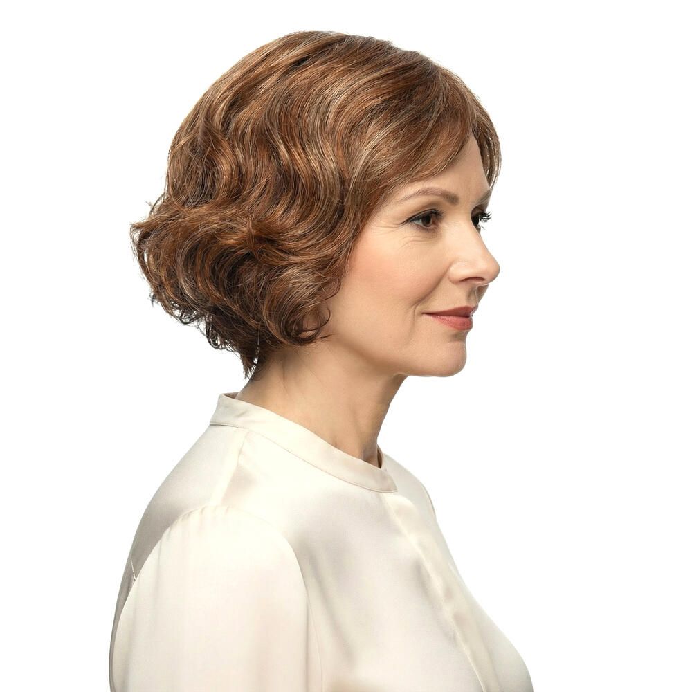 Frau mit brauner Perücke mit Pony. Die Perücke hat blonde Strähnen und welliges Haar. Sie trägt ein weißes Hemd.