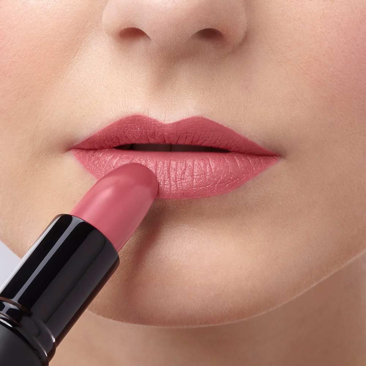 Person trägt rosafarbenen Lippenstift auf die Lippen auf. Schwarzer Lippenstift-Hülse sichtbar.