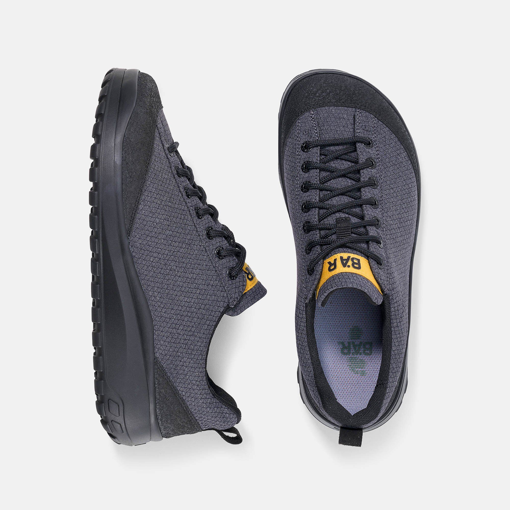 Draufsicht auf zwei graue Herren-Schnürschuhe. Schwarze Sohlen, Schnürsenkel und Details. Gelber Schriftzug BÄR.