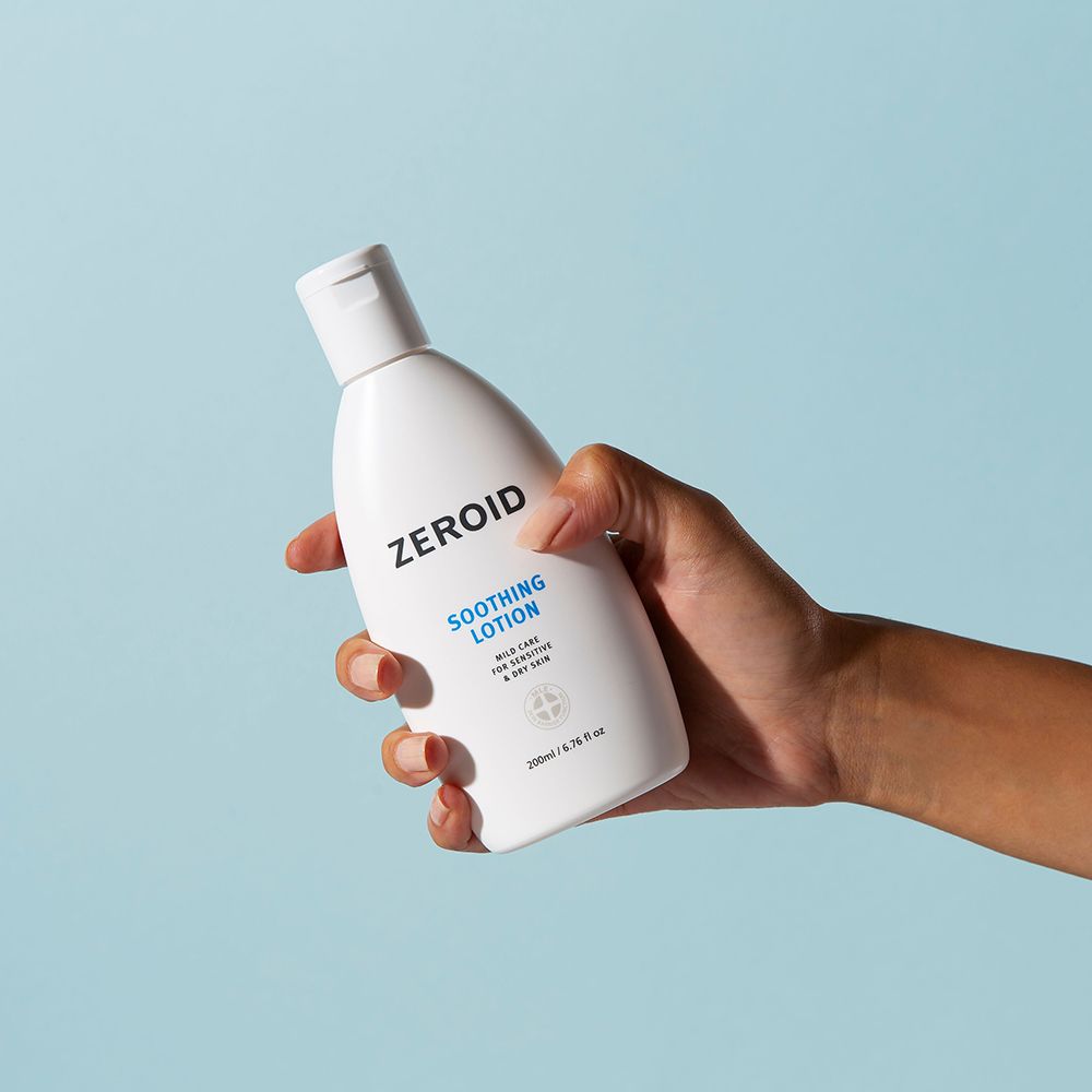 Weiße Flasche mit Klappverschluss, gehalten von einer Hand. Aufschrift: ZEROID, Soothing Lotion. 200ml/6.76 fl oz. Blauer Hintergrund.