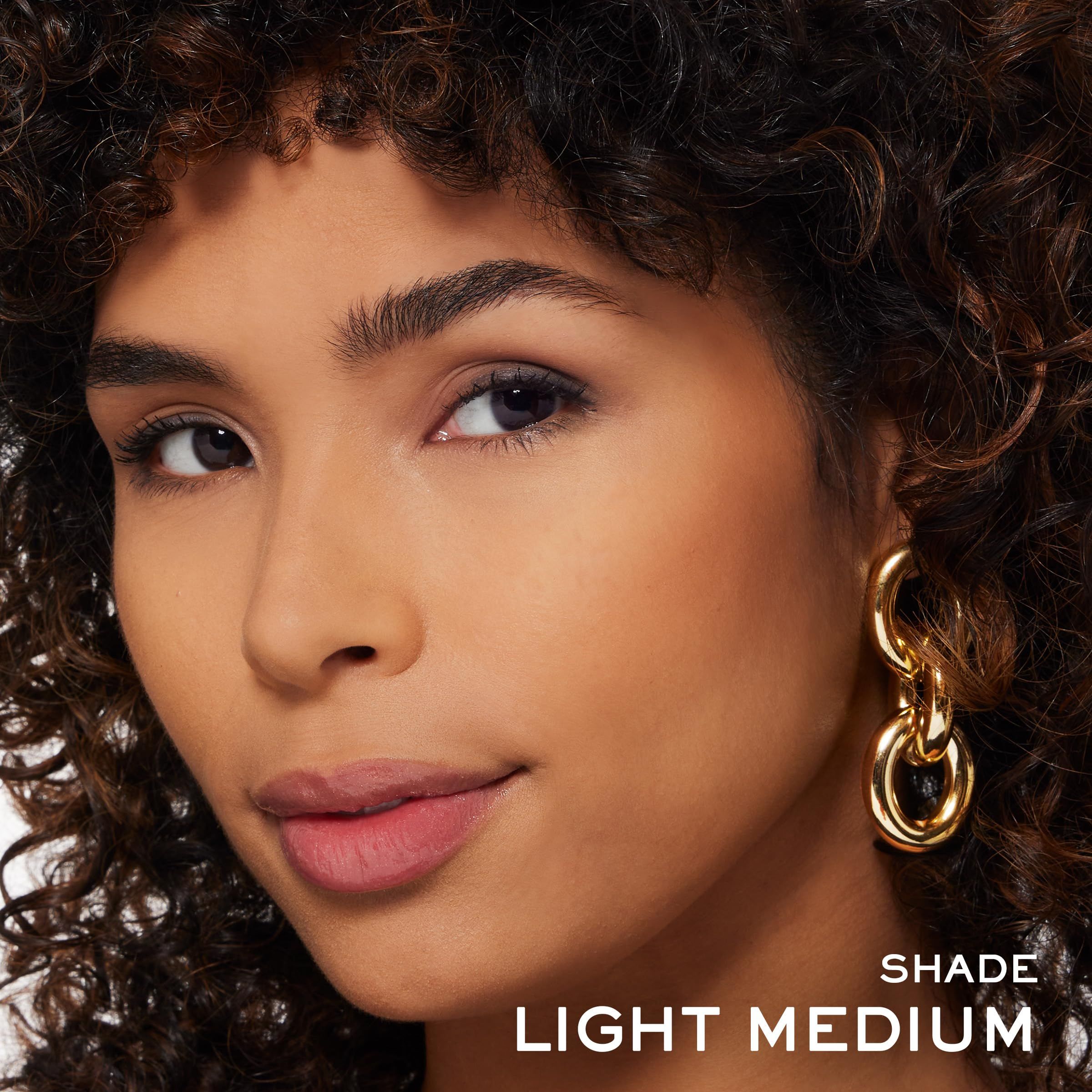 Nahaufnahme eines Gesichts. Hautton Light Medium. Frau mit Locken und goldenen Ohrringen. Text: SHADE, LIGHT MEDIUM.