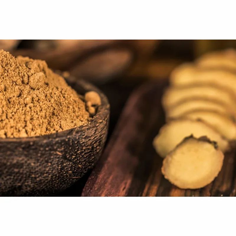 Schüssel mit braunem Pulver und geschnittener Ingwer. Holzbrett.