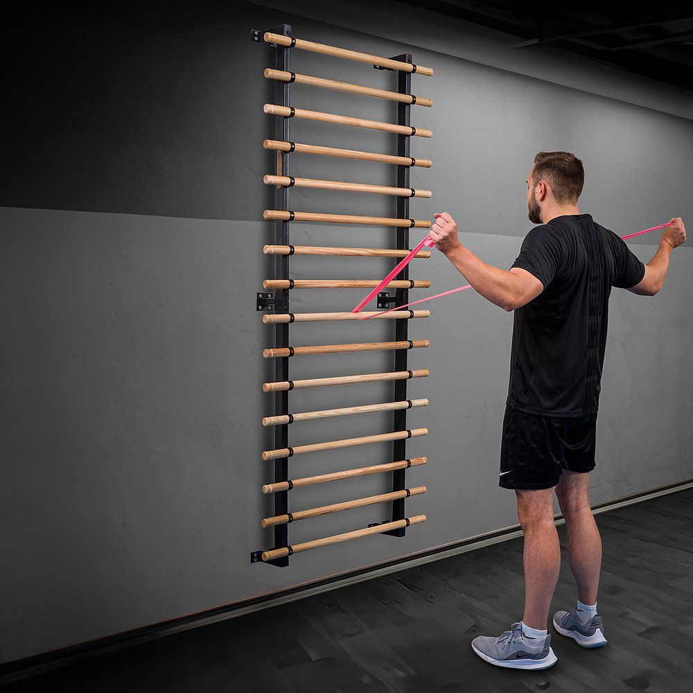 Mann mit Theraband an Sprossenwand. Er trainiert. Schwarzer Rahmen, Holzsprossen.