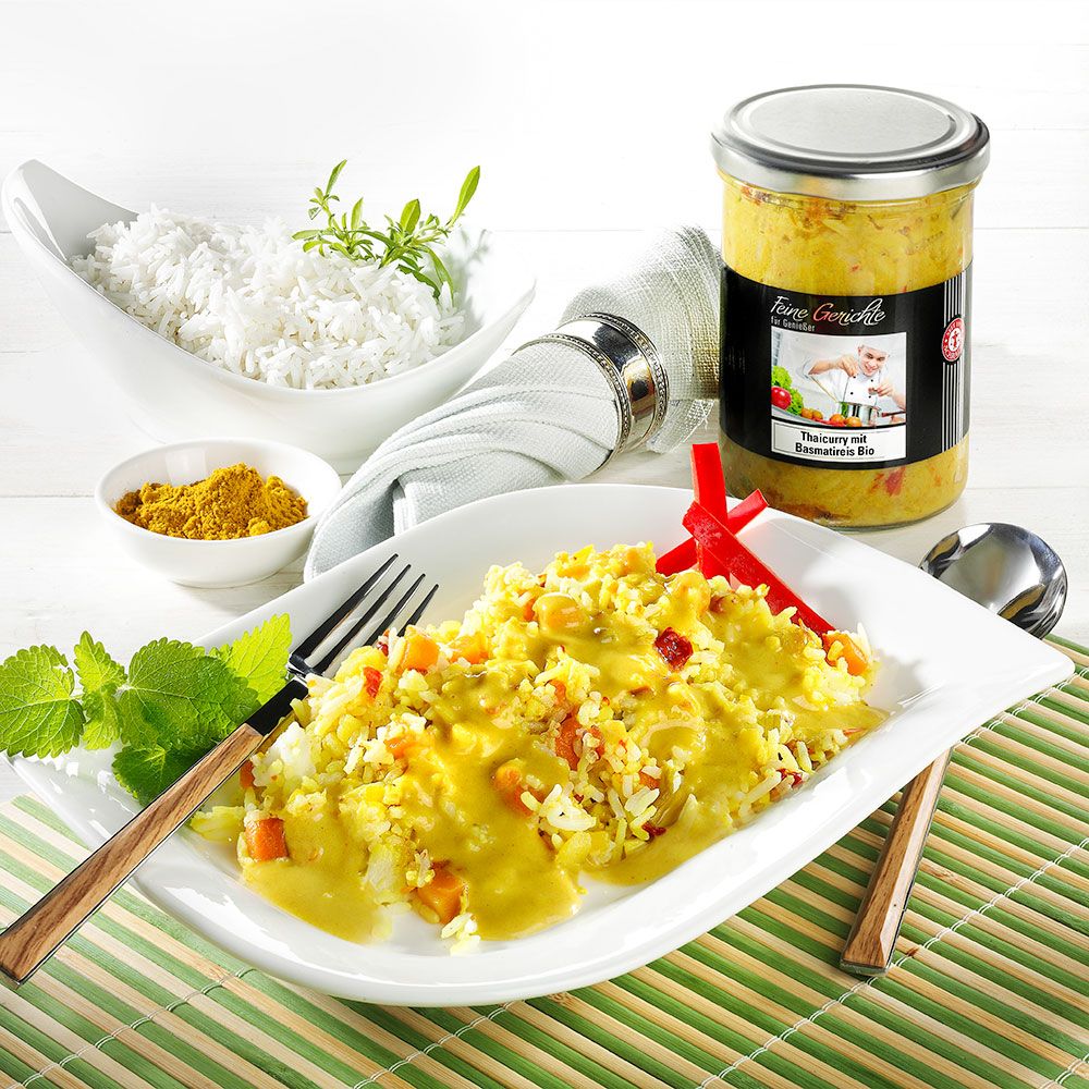 Teller mit Curry und Reis, daneben Reis in Schale, Currypulver, Glas mit Curry.