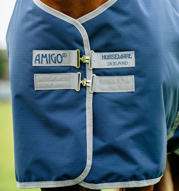 Nahaufnahme der blauen Pferdedecke. Graue Riemen mit silbernen Schnallen. Logos Amigo und Horseware Ireland.
