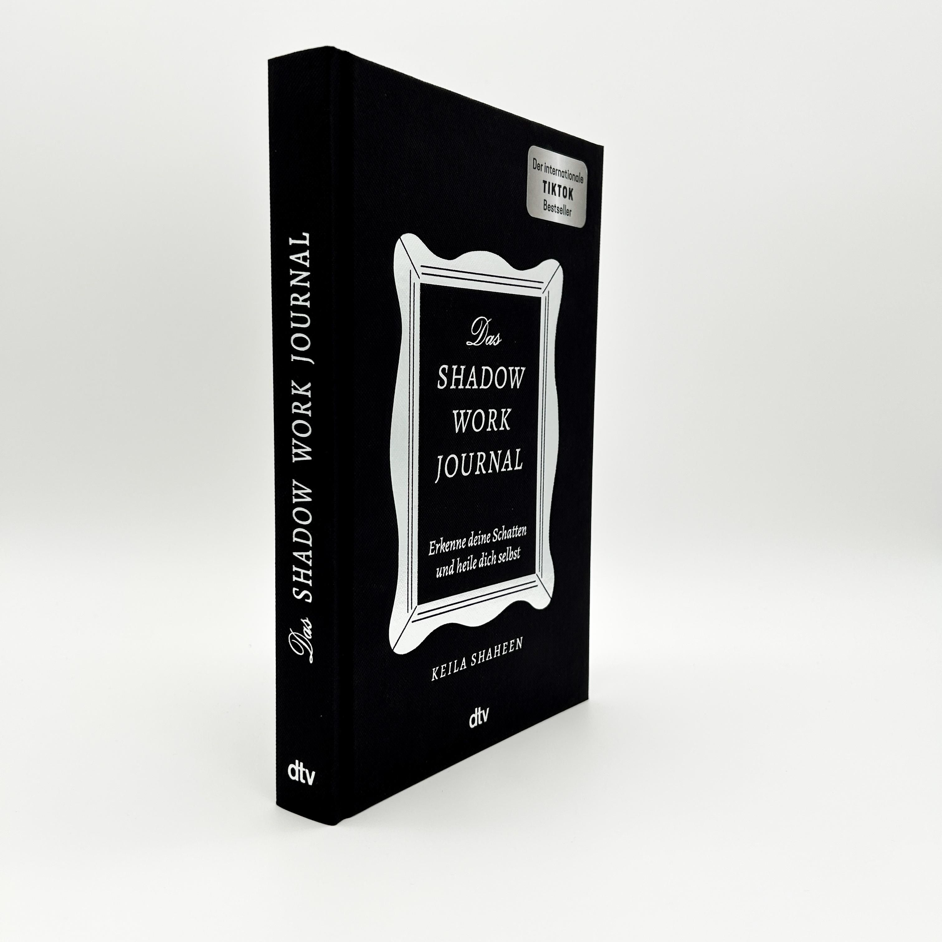 Buch "Das Shadow Work Journal" im 3/4-Profil. Schwarzer Einband, silberner Rahmen, weißer Titel. Autor: Keila Shaheen. Verlag: dtv. TikTok Bestseller-Aufkleber.