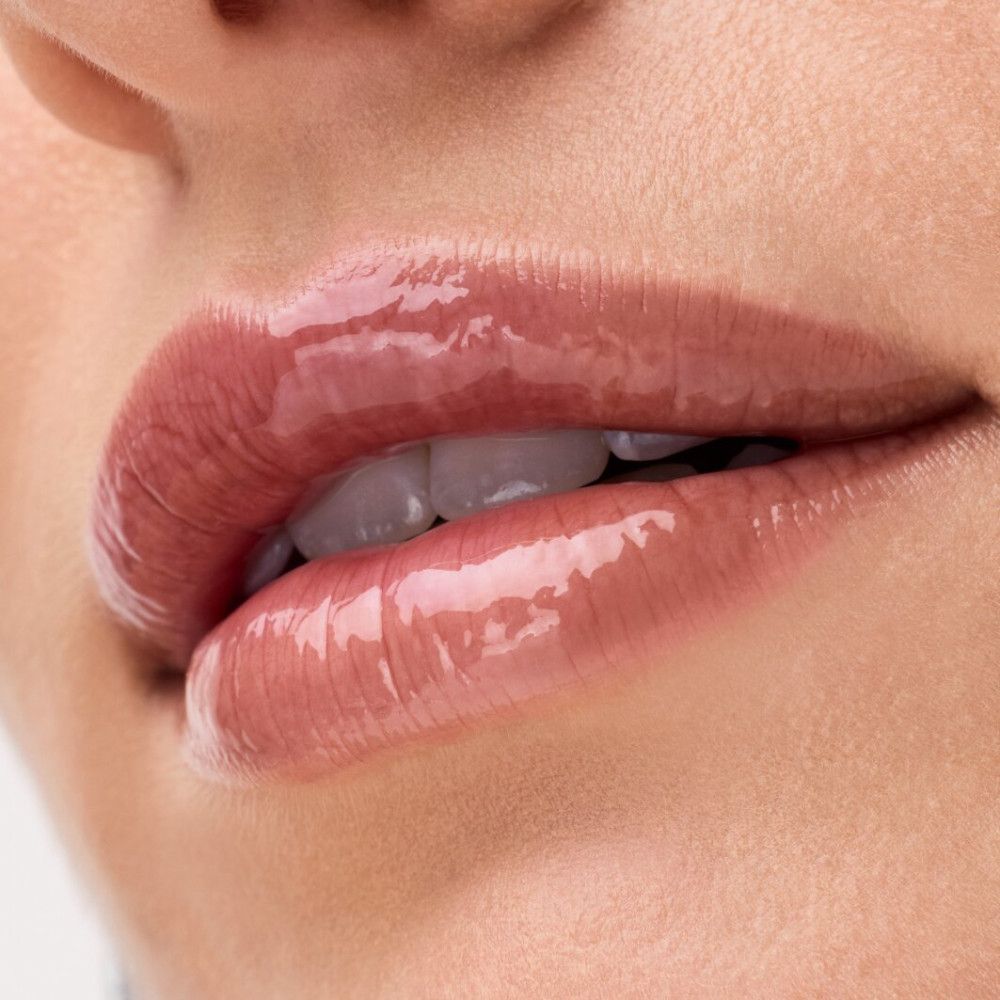 Nahaufnahme von Lippen mit glänzendem Lippenbalsam. Helle Haut. Zähne sichtbar.