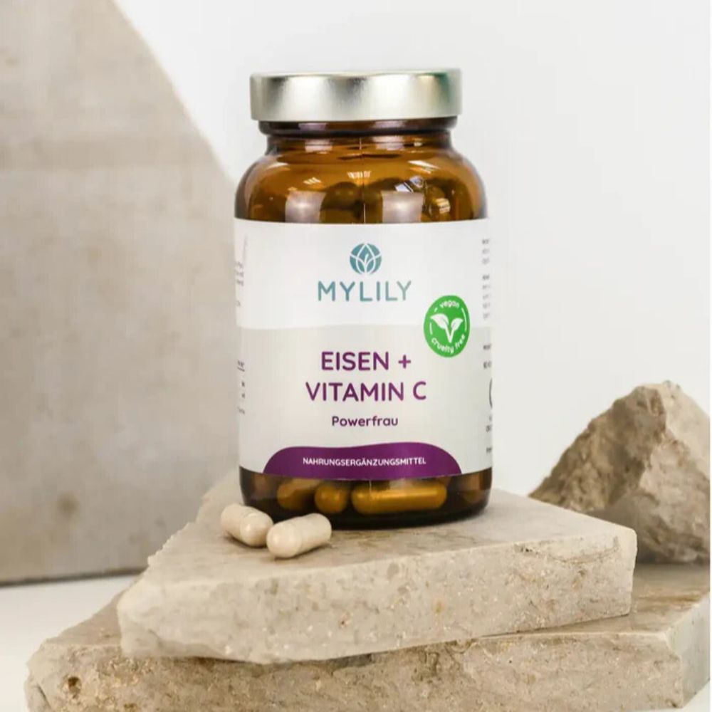 Braune Flasche mit Kapseln auf Stein. Aufschrift: MYLILY, Eisen + Vitamin C, Powerfrau. Nahrungsergänzungsmittel.