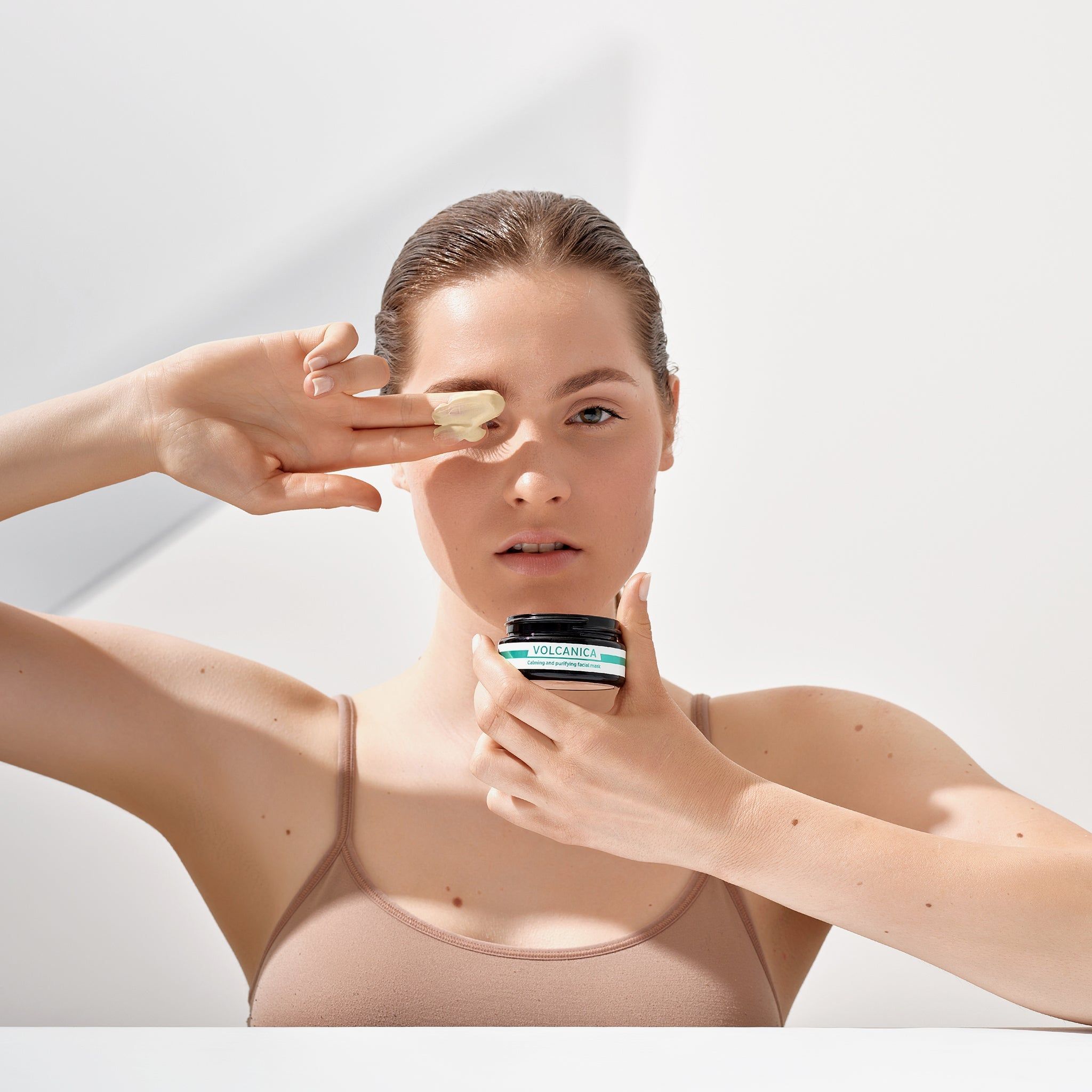 Frau hält Tiegel und trägt Maske auf. Produkt: VOLCANICA. Helle Haut, Tanktop.