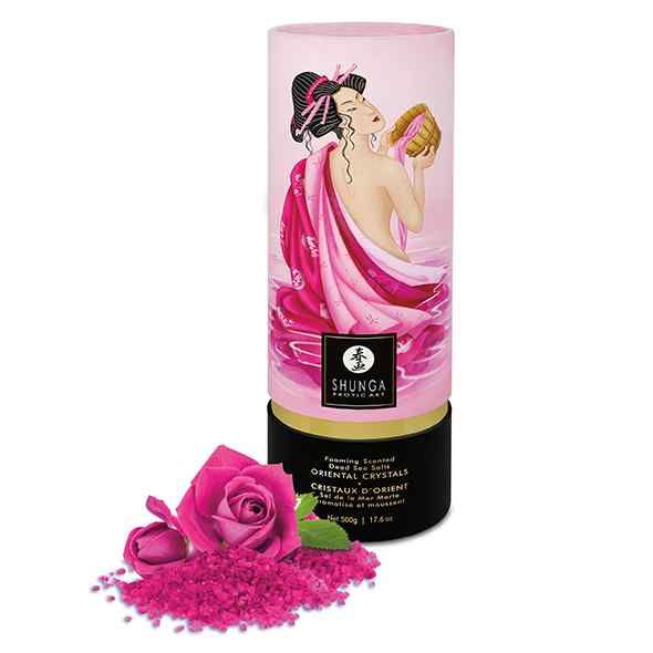 Rosa zylindrischer Behälter mit Frau und Produktnamen. Daneben pinkfarbene Kristalle und eine Rose.