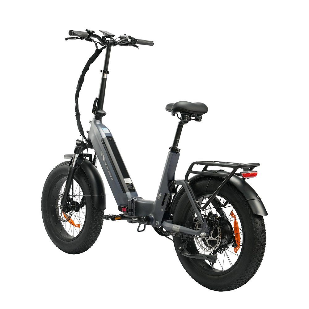 Graues Klapp-E-Bike mit schwarzen Reifen und orangefarbenen Akzenten. Das Fahrrad hat einen Gepäckträger und hydraulische Scheibenbremsen.