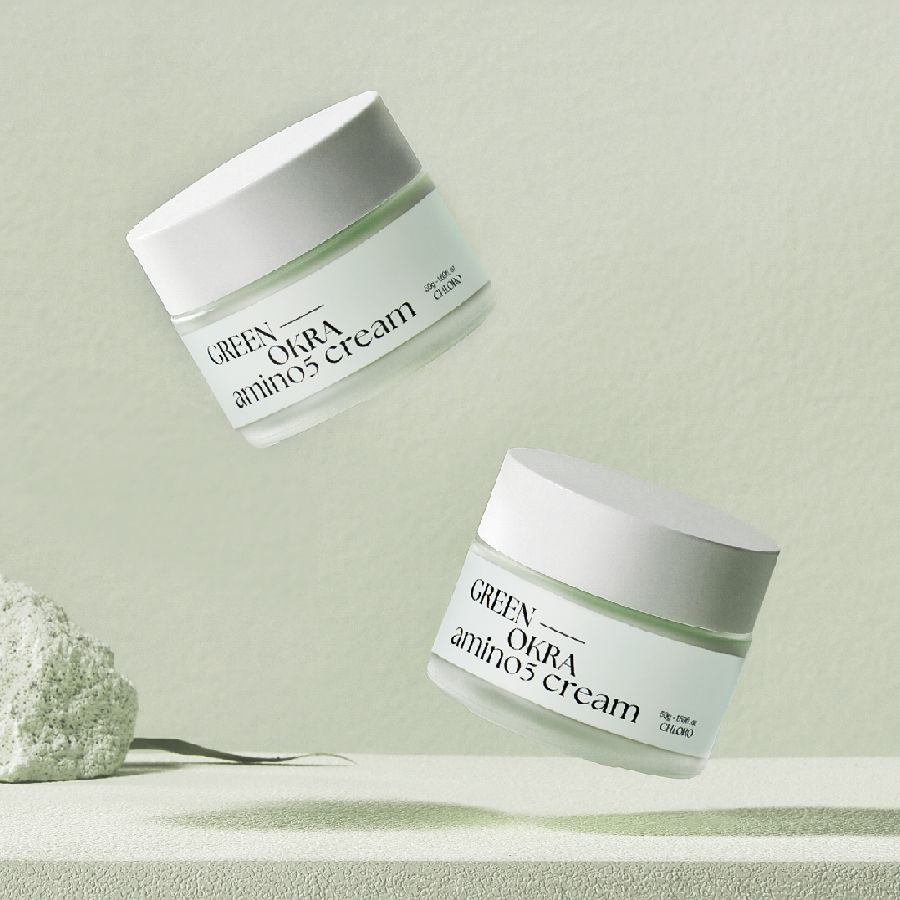 Zwei schwebende Creme-Gläser mit weißen Deckeln. Aufschrift: GREEN OKRA amino5 cream. Hintergrund grün.