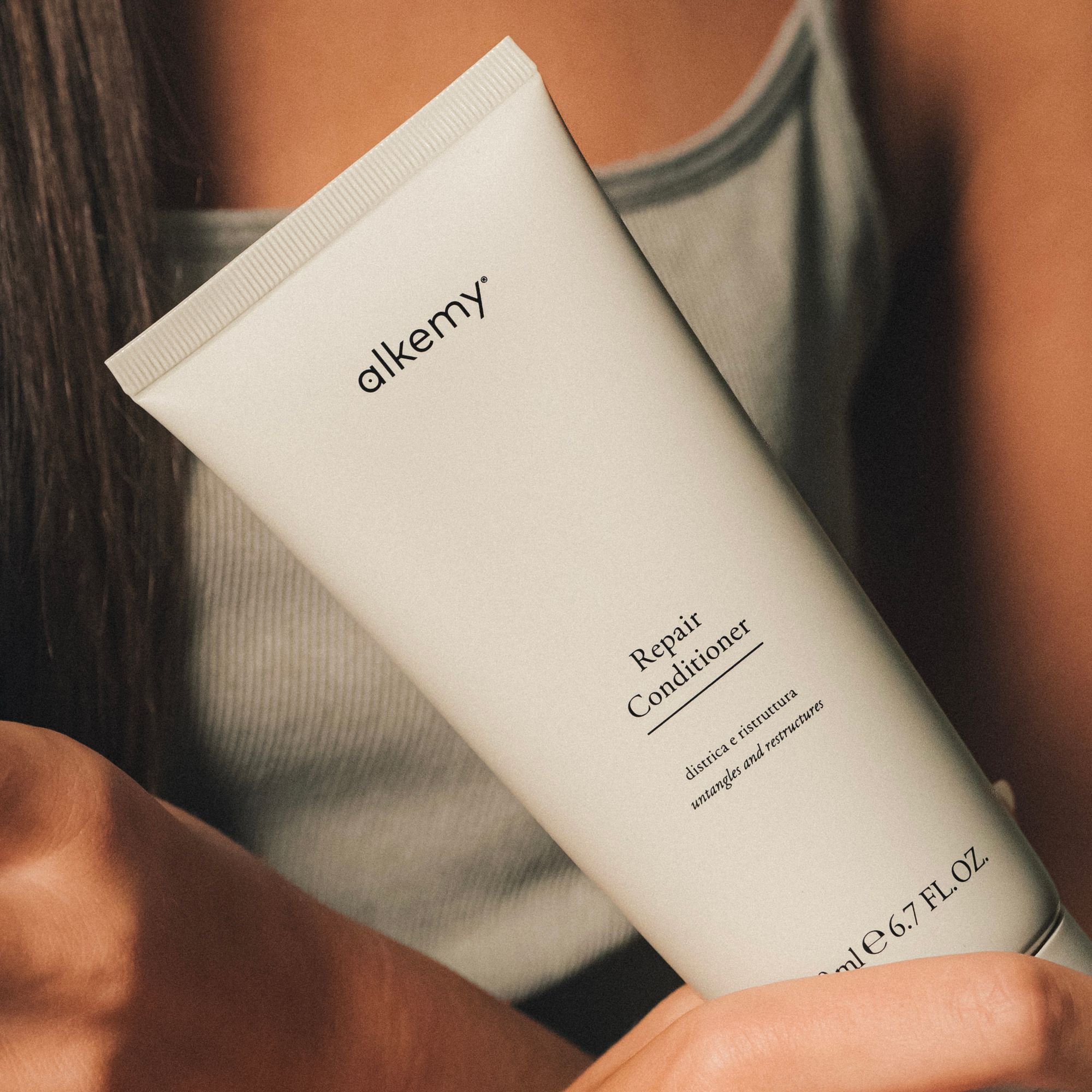 Eine Flasche Alkemy Repair Conditioner, 200 ml, wird von Händen gehalten.