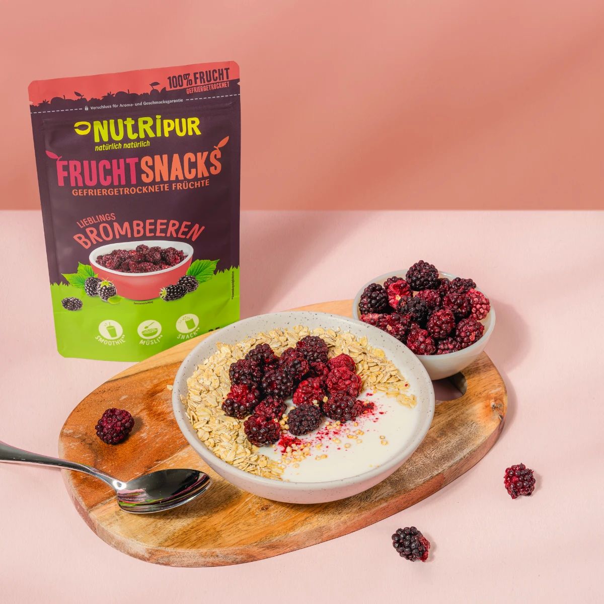 Brombeeren auf Joghurt und Müsli in einer Schale. Daneben eine Packung NutriPur Frucht Snacks und eine Schale mit Brombeeren.