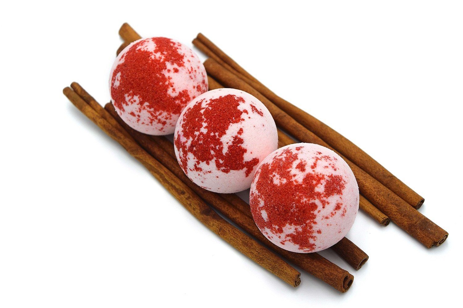 Drei runde, rosa Badebomben mit roten Flecken, auf Zimtstangen platziert. Auf weißem Hintergrund.